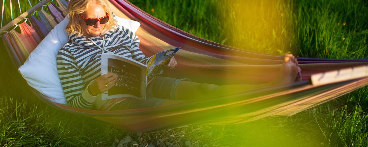A woman lying in a hammock reading a magazine