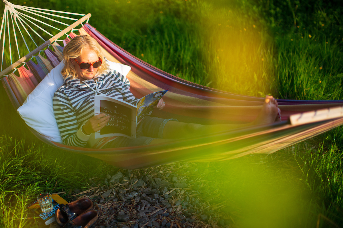 A woman lying in a hammock reading a magazine