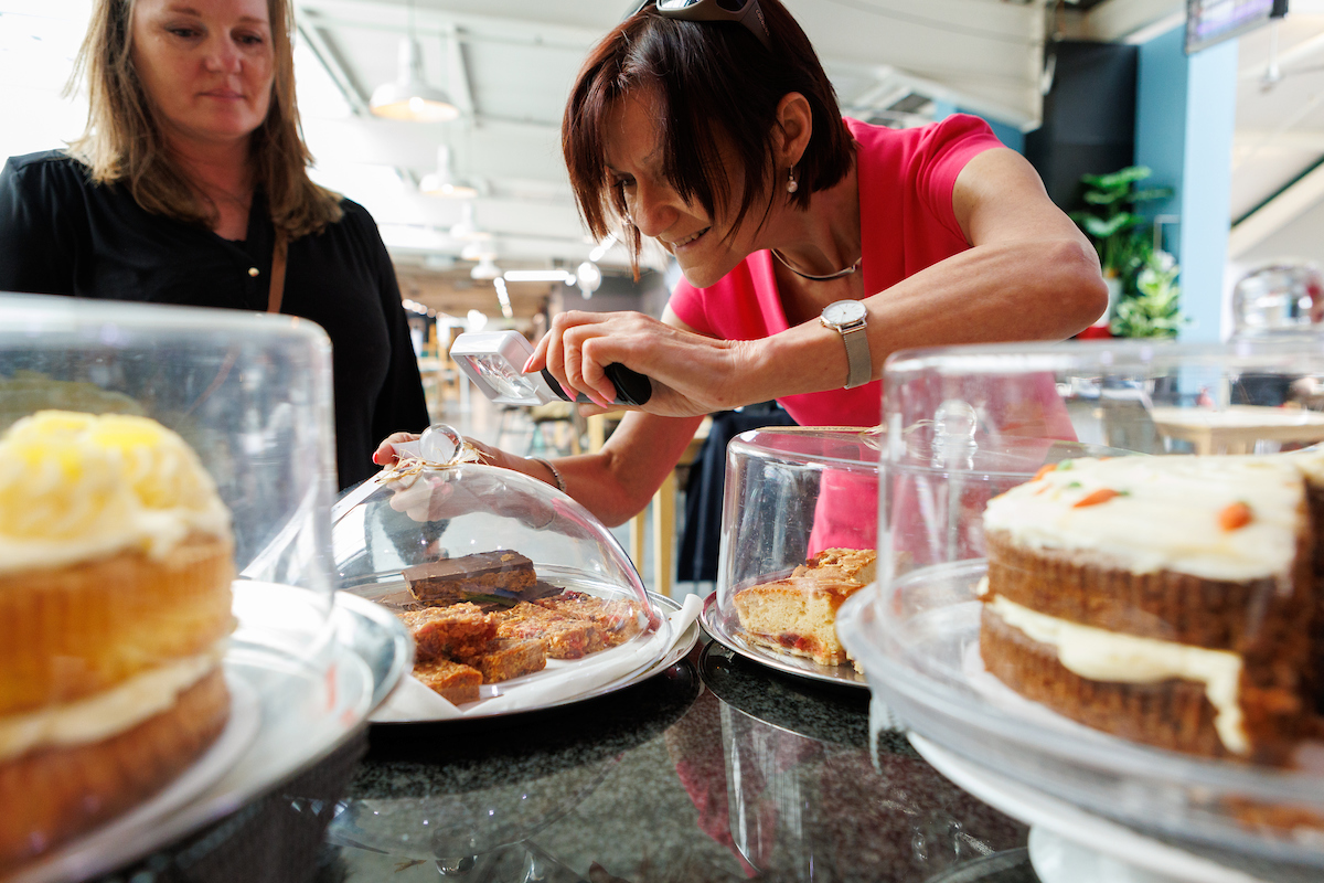 A visually impaired woman using a magnifier to look at the label on a cake whilst in a cafe.