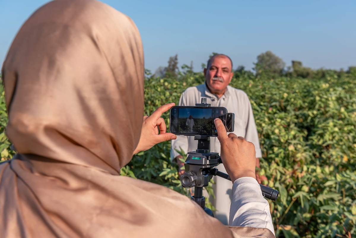 A lady using a smartphone to film an interview with a farmer in a field